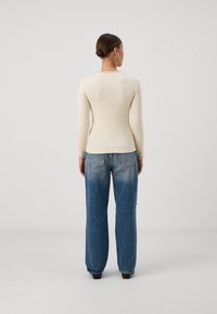Long-sleeve cream top with ribbed texture and frilled neckline, paired with light blue, wide-leg, faded denim jeans with back pockets.