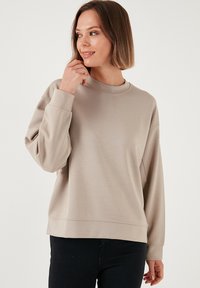 Felpa leggera color beige chiaro con scollo a rotondo, spalle basse e polsini a costine. Realizzata in tessuto liscio e morbido con una vestibilità comoda.