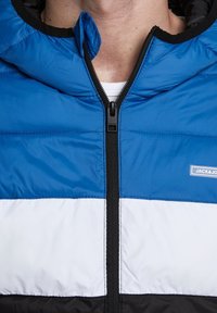 Blauwe, witte en zwarte gewatteerde jas met ritssluiting, voorzien van een hoodie en logo-embleem. Glad, gewatteerd materiaal met contrasterende kleuren.