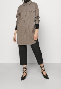 Brun ullklänning med knappfront och två bröstfickor, som matchas med svarta vida byxor och svarta spetsiga lägenhetsdojor med rem.