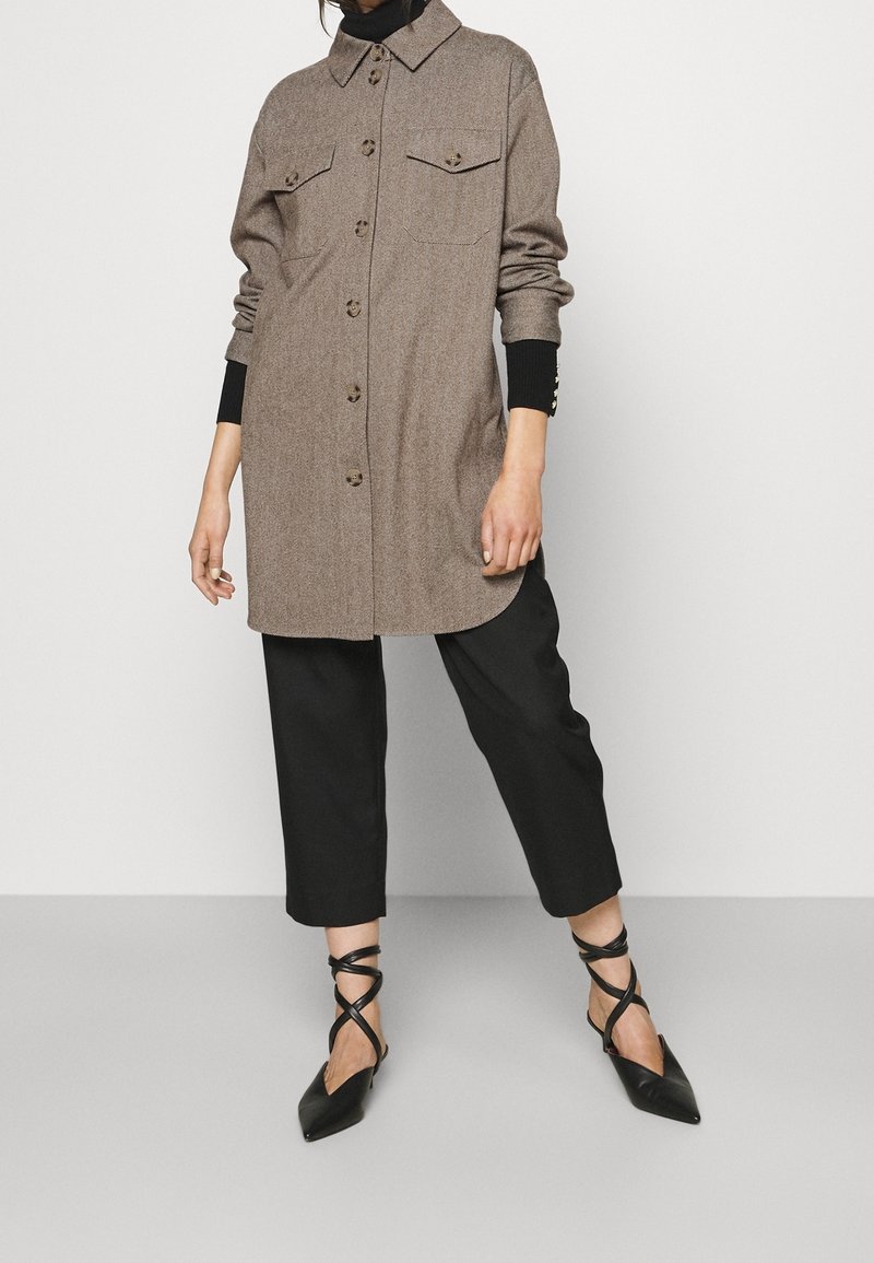 Brun ullklänning med knappfront och två bröstfickor, som matchas med svarta vida byxor och svarta spetsiga lägenhetsdojor med rem.