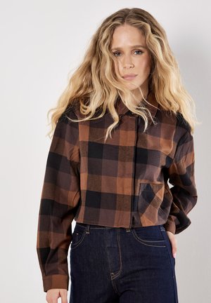 Brown and black plaid cropped shirt with a button-up front, a pointed collar, and a single chest pocket. Features long sleeves and soft texture.