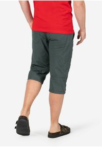 Graue, strukturierte Caprihosen mit schlankem Schnitt, umgeschlagenen Säumen und zwei Gesäßtaschen. Getragen mit braunen Riemchensandalen. Rotes Hemd teilweise sichtbar.