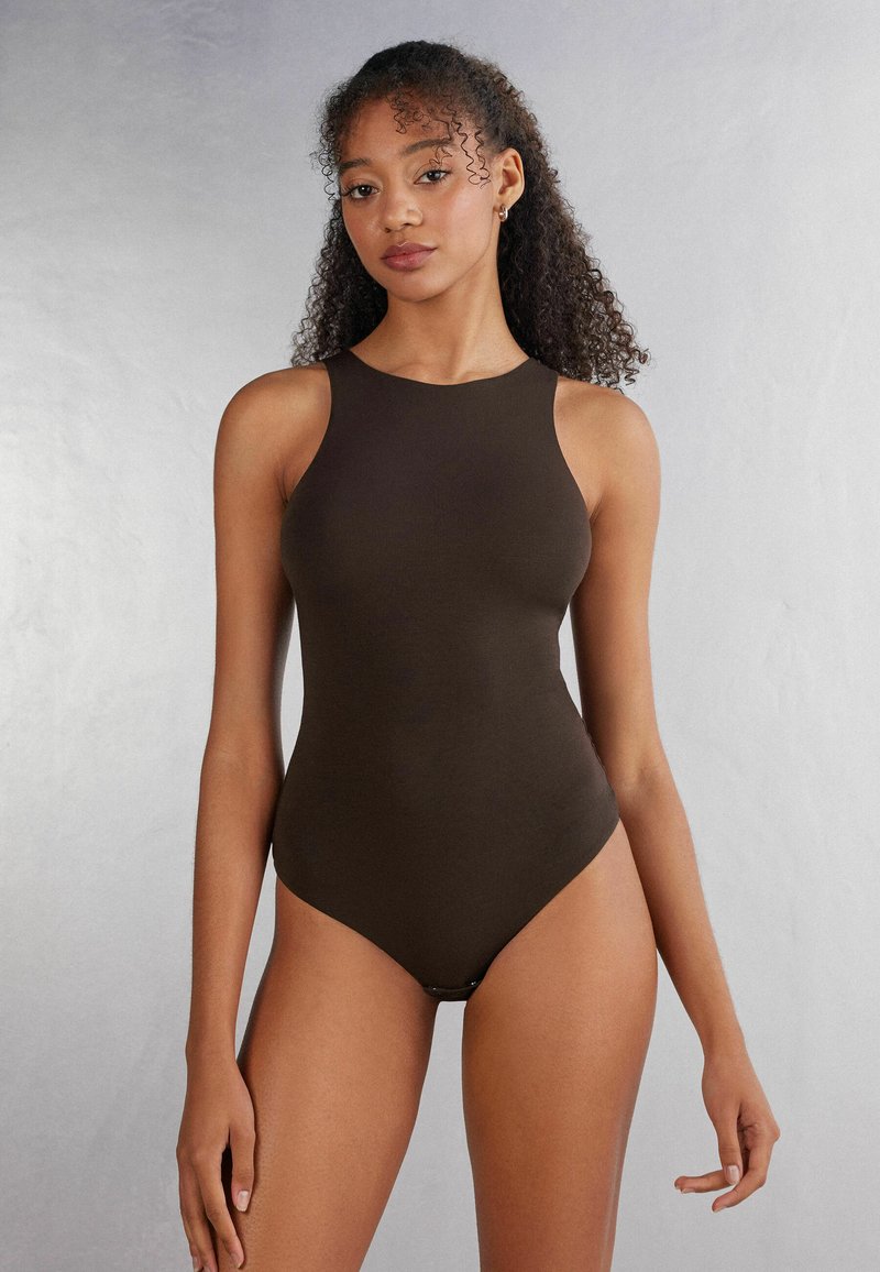 Bruine mouwloze bodysuit met hoge hals, nauwsluitend ontwerp en naadloze afwerking. Gladde textuur met een uitsnijding op de onderrug.