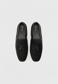 Schwarze Wildleder Slipper mit glatter Oberfläche, ausgestattet mit einem dekorativen Schleifenakzent und einem weichen Futter. Abgerundete Zehenform mit dezenten Nähten.