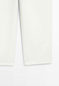 Sezione inferiore di pantaloni bianchi a gamba dritta che mostrano l'orlo e i dettagli della cucitura laterale su uno sfondo bianco uniforme.