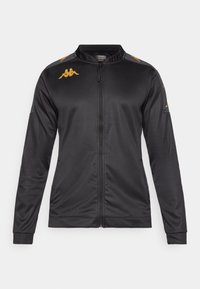 Veste de sport noire zippée faite en tissu lisse. Dotée d'un col montant, de manches longues et de logos dorés sur les épaules.