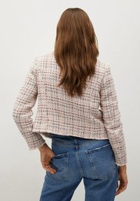 Rosa Tweed-Jacke mit strukturierter Oberfläche, kurzem Schnitt und langen Ärmeln, kombiniert mit mittelblauen Jeans mit Gesäßtaschen.