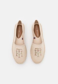 Espadrilles beige à enfiler avec des semelles tissées, décorées d'un logo multicolore Tommy Hilfiger sur le dessus et du nom de la marque à l'intérieur.