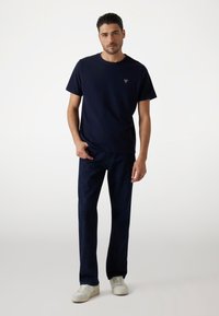 Mørkeblå bomulds T-shirt med rund halsudskæring og et diskret logo. Matchet med mørkeblå denim jeans og hvide sneakers.