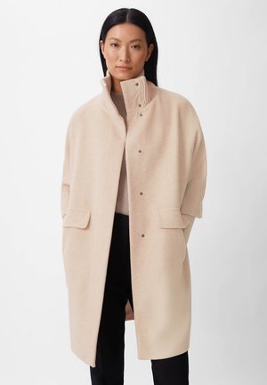 Beige Wollmantel mit hohem Kragen, Druckknopfverschluss und Seitentaschen; zeichnet sich durch eine entspannte Silhouette und eine weiche Textur aus.
