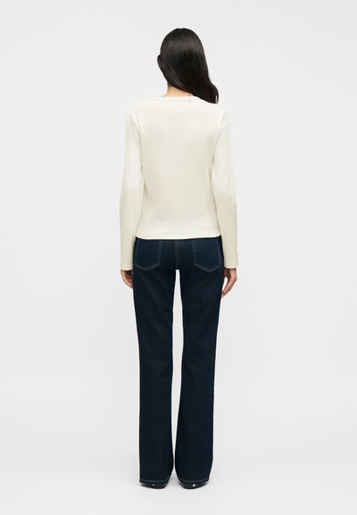 Κρεμ μακρυμάνικη μπλούζα σε συνδυασμό με σκούρο μπλε τζιν με φαρδείς παντελόνια. Λείο υφασμάτινο ύφασμα, απλός σχεδιασμός και εφαρμοστή γραμμή με ορατές ραφές στο πίσω μέρος.