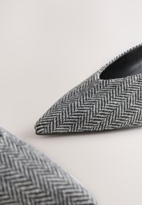 Houndstooth rašto smailiakių batų, pagamintų iš tekstūruotos pilkos ir juodos medžiagos, su elegantišku, žemai nupjautu dizainu ir juoda pamušalu.