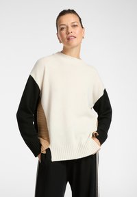 Sweter dzianinowy z kremowym korpusem, czarnymi rękawami i ribbowym beżowym bokiem. Okrągły dekolt i ribbowe wykończenie dołu tworzą kontrast tekstur.