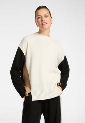 Gebreide trui met een crèmekleurig lichaam, zwarte mouwen en een ribbelige beige zijkant. De ronde halslijn en ribbelige zoom zorgen voor een tekstuurcontrast.
