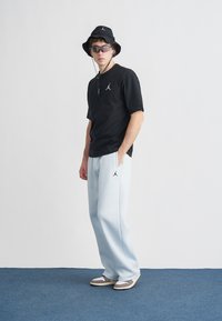 Svart kortermet skjorte med logo, lyseblå joggebukser, svart bøttehatt og solbriller, med avslappet passform og sporty design.