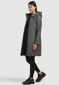 Grijze waterdichte jas met een capuchon, drukknoopsluiting en zijzakken. Gecombineerd met zwarte leggings en sneakers voor een casual uitstraling.