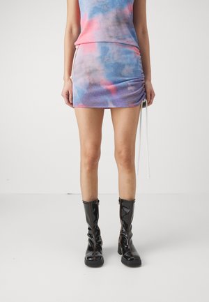Tie-dye crop top and mini skirt in blue, pink, and purple tones; features ruched detailing and a drawstring. Black knee-high zip-up boots.