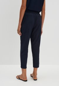 Pantalons légers bleu marine avec une taille élastique, des jambes fuselées et des ourlets retroussés. Pas de poches visibles. Texture lisse.