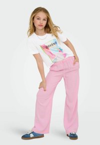 White t-shirt with a colorful "Havana" graphic, paired with light pink wide-leg trousers and blue sneakers with white accents.