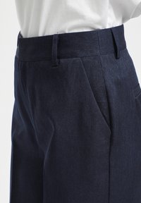 Pantalon bleu marine sur mesure avec une texture lisse, doté d'un devant plat et de poches latérales, fabriqué en tissu de haute qualité pour une grande durabilité.