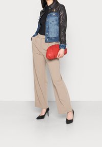 Giacca in denim e pelle con una combinazione di colori blu e nero, pantaloni beige a vita alta, pochette rossa e scarpe nere con tacco alto.