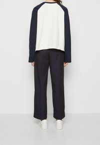 Marineblaue und cremefarbene langärmlige Hemd mit Raglan-Design, kombiniert mit weiten marineblauen Hosen und weißen Sneakers. Einfaches und lässiges Outfit.