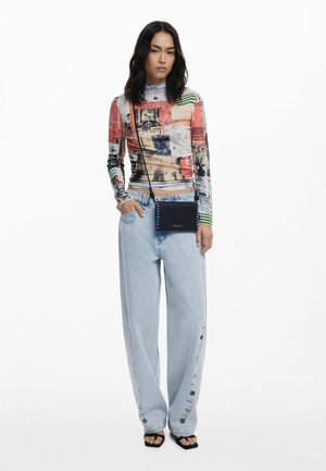 Langärmliges, eng anliegendes Oberteil mit einem bunten Patchwork-Design, kombiniert mit hellblauen, weit geschnittenen Jeans mit Knopfakzenten und einer schwarzen Umhängetasche.