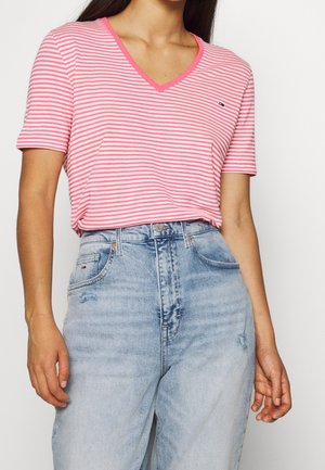 Kobieta ubrana w różowo-biały, pasiasty T-shirt z dekoltem w serek, włożony w jasnoniebieskie jeansy z wysokim stanem i lekkim postarzaniem na kieszeniach.