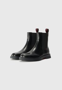 Black leather ankle boots with elastic side panels, rounded toes, and rubber soles. Featuring red pull tabs on the back.