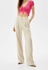 Rosa kortärmad topp med ribbad textur och knytdetalj fram, tillsammans med ljusbeiga vida byxor med knapp och veck.