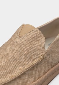 Μπεζ παπούτσι χωρίς κορδόνια με υφασμάτινη υφή πλεκτού, ελαστική ένθεση στο άνω μέρος και επενδεδυμένη άκρη της σόλας για καθημερινή χρήση.