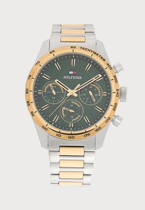 Montre-bracelet Tommy Hilfiger avec bracelet métallique or et argent, cadran vert foncé, trois sous-cadrans et échelle tachymétrique sur la lunette dorée.