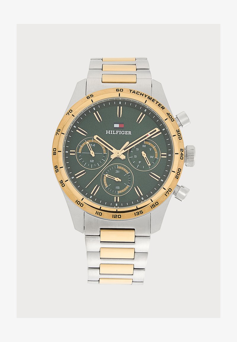 Ρολόι χειρός Tommy Hilfiger με μεταλλικό μπρασελέ σε χρυσό και ασημί, σκούρο πράσινο καντράν, τρεις υποδιαβάσεις και ταχυμετρική κλίμακα στη χρυσή στεφάνη.