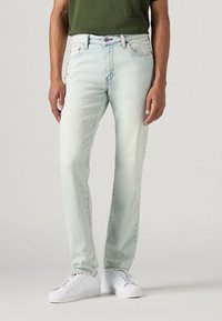 Lyseblå jeans laget av denim, med rett ben design, fem lommer og en glidelås med knappelukking. Kombinert med hvite joggesko.