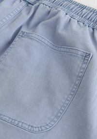 Tissu bleu clair avec une ceinture élastique et une poche carrée ornée de doubles coutures renforcées.