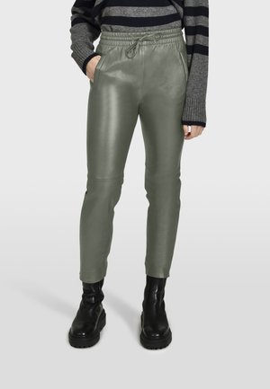Pantalons en simili cuir vert avec une coupe ajustée, une taille élastique et des poches latérales, associés à des bottes noires à semelles épaisses.