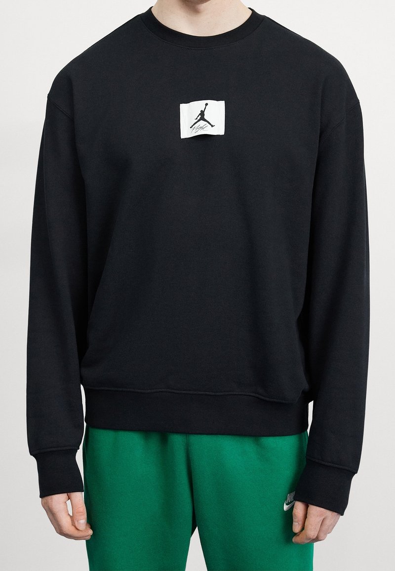 Sudadera negra con cuello redondo, mangas largas y un parche del logo de Jordan en blanco en el frente. Tela suave y texturizada; ajuste relajado.
