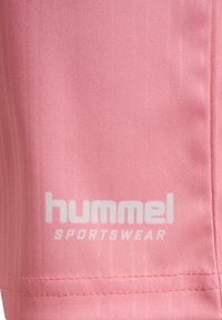 Rosa sportklädesmaterial med en slät textur har en vit "hummel"-logotyp och texten "SPORTSWEAR" i nedre högra hörnet. Sömmarna är snyggt avslutade.