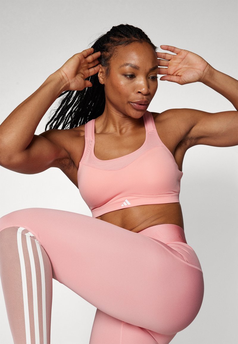Soutien-gorge de sport rose clair et leggings, dotés d'une texture lisse, d'un design dos nageur et de trois bandes blanches sur les jambes.