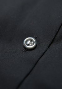 Close-up van zwart stof met een metalen knop met een glanzende zilveren afwerking, stevig gestikt met zichtbare draad, die de textuur benadrukt.