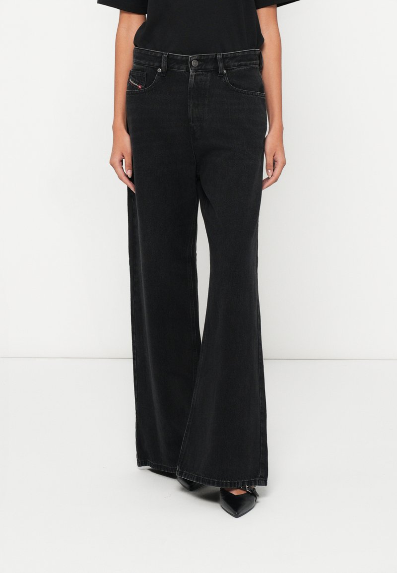 Μαύρα τζιν με φαρδύ πόδι και ψηλή μέση, με εμπρόσθιες τσέπες και διακριτική κόκκινη ραφή. Λείο, υφασμάτινο ύφασμα με υφή.