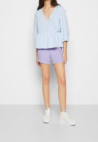Niebiesko-biały bluzka w kratę z peplum, w połączeniu z lawendowymi szortami. Modelka ma na sobie białe sneakersy za kostkę.