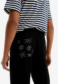 Pasiasty granatowo-biały T-shirt, krótki rękaw, zestawiony z czarnymi spodniami z haftowanymi kwiatowymi wzorami na tylnym kieszeni.
