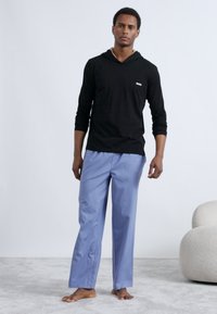 Must pika varrukaga dressipluus logoga, mille juurde kuuluvad helesinised lahtised püksid. Sile tekstuur, vabaaja disain ja nähtavad mustrid puuduvad.