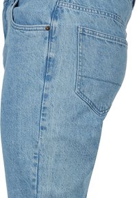 Jean en denim bleu clair montrant la couture latérale et la poche arrière avec un détail de rivet, porté à la hanche d'une personne.