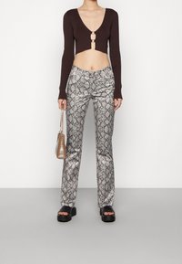 Brązowy prążkowany krótki top z głębokim dekoltem w kształcie V i okrąłym detalem, zestawiony z srebrnymi spodniami w wężowy wzór z szerokimi nogawkami oraz czarnymi sandałami na platformie.