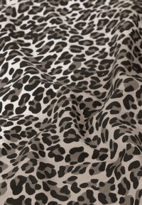 Tissu imprimé présentant un fond beige avec un motif de taches de léopard noires. La texture semble douce et légèrement froissée.