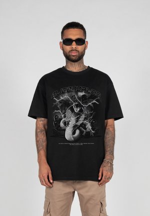 Svart bomull T-skjorte med grafikk av en slange og lyn. Avslappet passform med korte ermer og rund hals. Beige cargo-shorts. 
