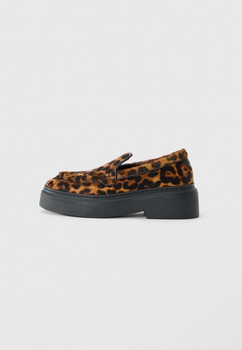 Scarpa in stile mocassino con tomaia in stampa leopardata marrone e nera e spessa suola piatta nera su sfondo bianco.